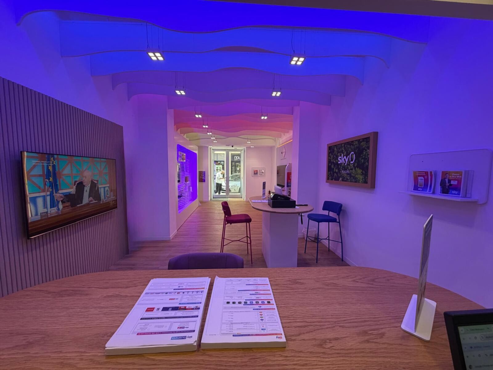 Sala principale dello store di Taranto: bancone bianco, sgabelli magenta, parete TV, illuminazione viola.
